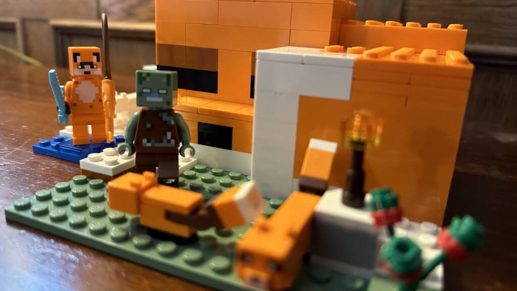 This is a photo of the LEGO Minecraft Fox Lodge Set. There are two Minifigures in the foreground, and in the background is a building which resembles a fox.