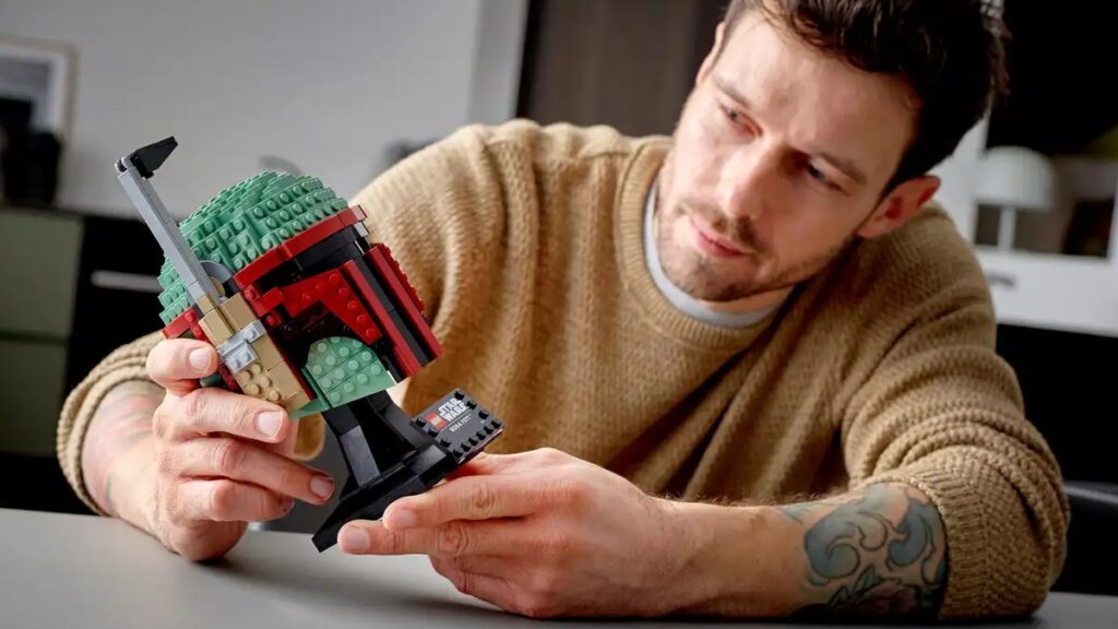 A man is holding a LEGO Star Wars (Boba Fett Helmet) in his hands and looking at the model.